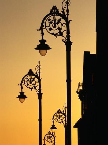 the silhouette of several street lights against an orange sky