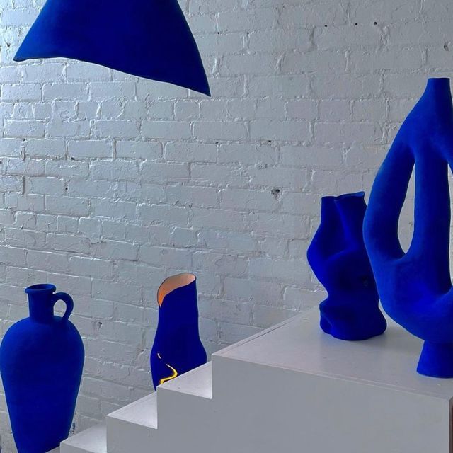 several blue vases are on display against a white brick wall, and one is upside down