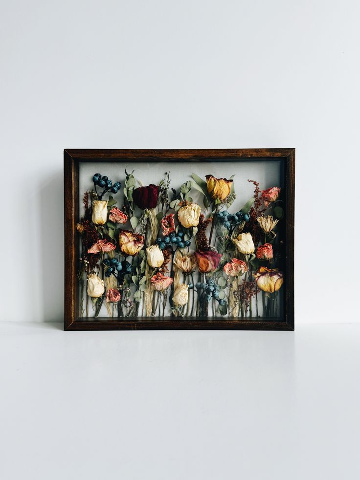 a wooden frame with flowers in it sitting on a table next to a white wall