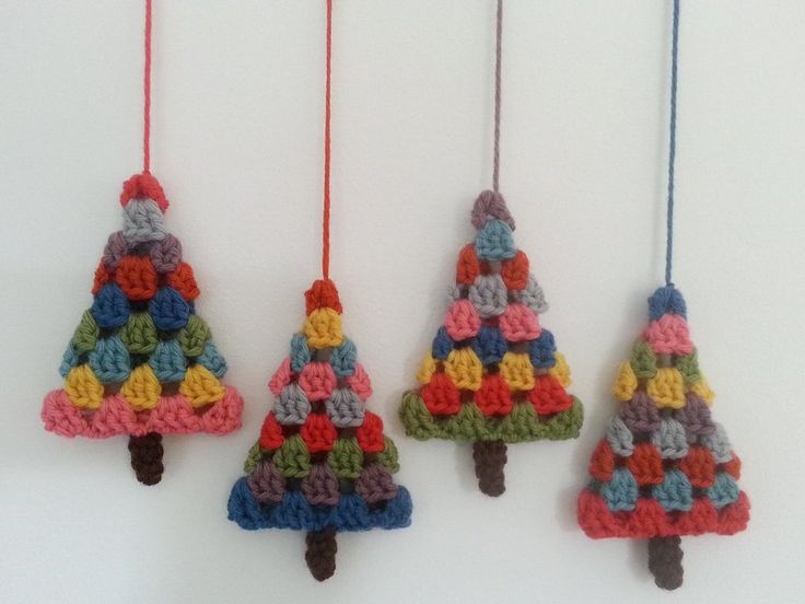 three crocheted christmas trees hanging from strings on a white wall with red, yellow, blue and green yarn