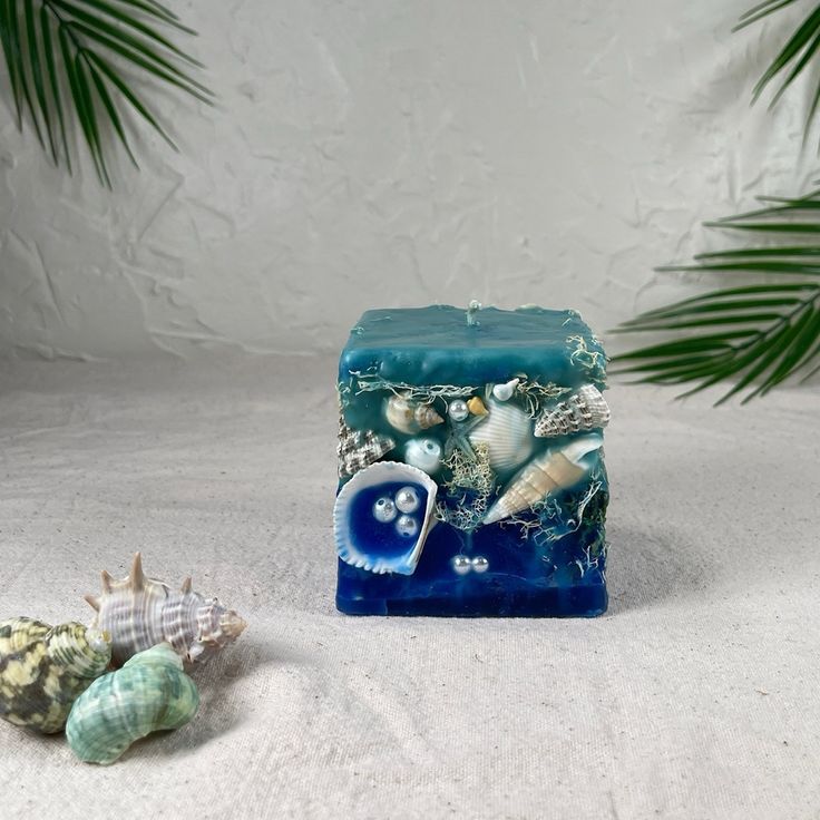 a blue square candle with shells and seashells around it