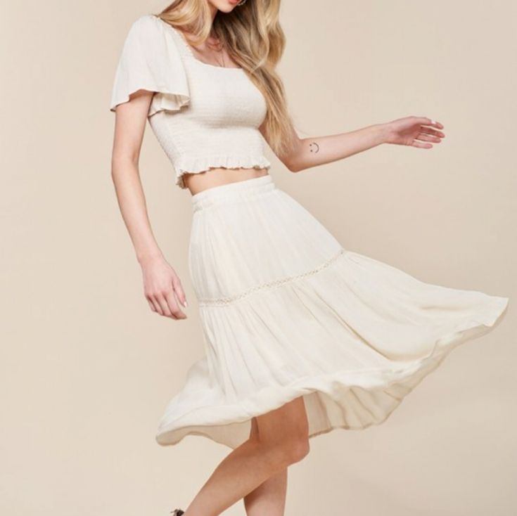 Elevate Your Summer Style With Our Woven Skirt Set In White! The Crop Top Features A Flattering Square Neckline And Smocking For A Perfect Fit, While The Flowy Sleeves And Ruffle Detail Add A Touch Of Charm. The Midi Skirt Has An Elastic Waistband And Lace Trim For A Feminine Touch, And Is Fully Lined For Comfort. Made Of 100% Rayon And 100% Polyester Lining. Model Is 5'8" And Wearing A Size Small. Fit: True To Size Pockets Skirt Lined Rayon Casual Ruffled Rayon Skirt, Off White Tiered Skirt For Spring, Spring Off-white Tiered Skirt, Spring Off White Tiered Skirt, Chic Off White Tiered Skirt, Chic Off-white Tiered Skirt, Cream Maxi Skirt With Elastic Waistband For Summer, Solid Rayon Skirt For Summer, Spring Off White Relaxed Fit Skirt