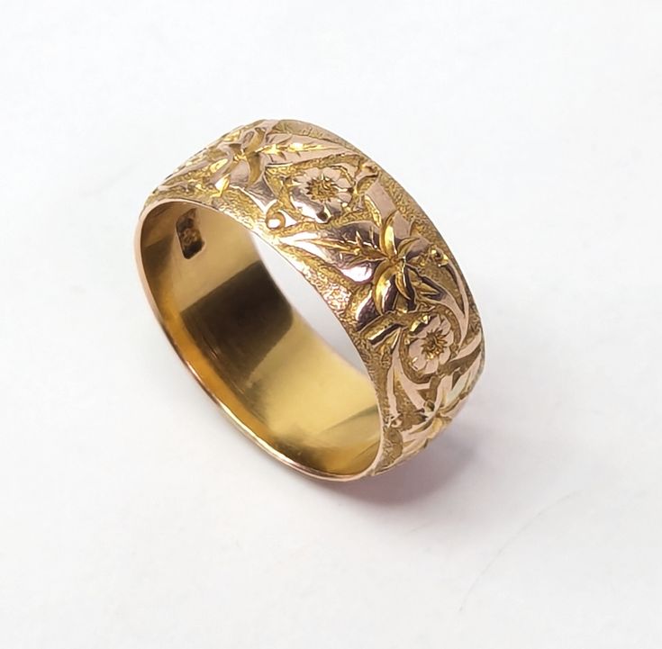 a gold wedding ring with intricate designs on the outside and inside, sitting on a white surface