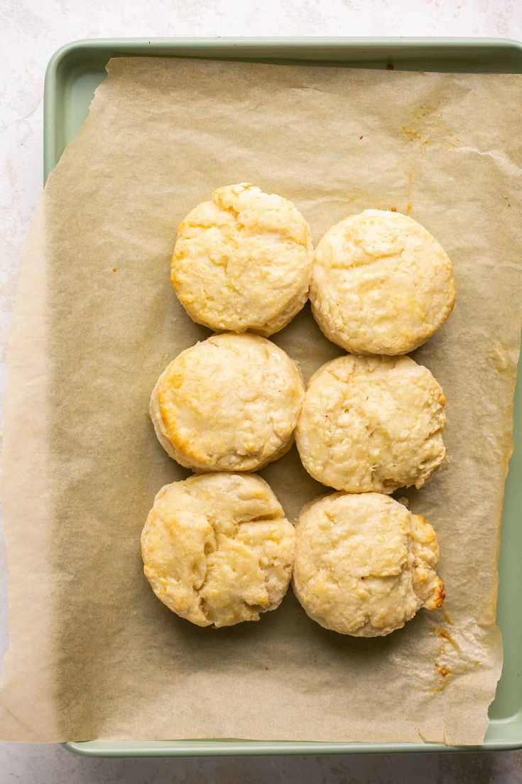 six biscuits sitting on top of a piece of parchment paper in a green tray next to a cup of coffee