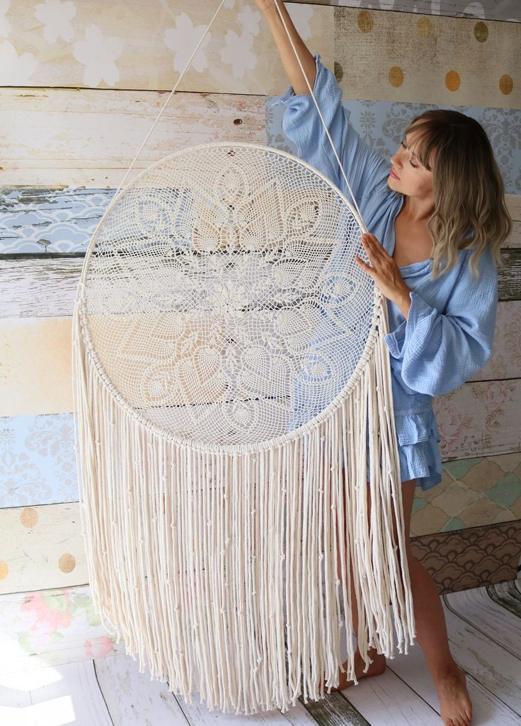 a woman is holding up a white dream catcher