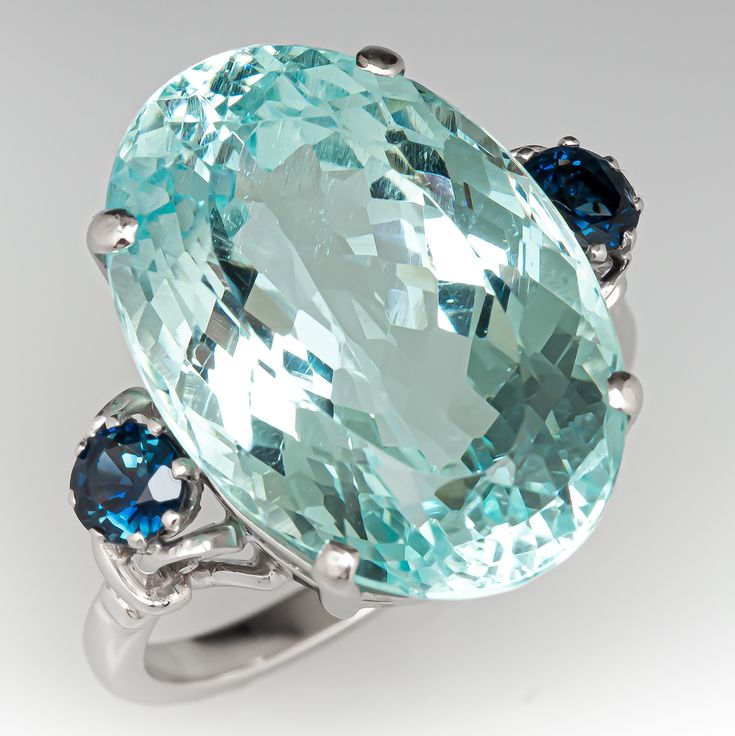 This captivating ring is centered with an oval cut aquamarine weighing 18.86 carats, in a four-prong setting. The shoulders are each prong set with one (1) round mixed cut sapphire. The ring measures 20.5mm at the top, rises 10.6mm above the finger, tapering to 2.1mm wide and 1.7mm thick at the base of the shank. Signed S & Co. and stamped with the modern UK, Birmingham assay office hallmarks. This ring is currently a size 9.25. Oval Aquamarine Ring, Uk Birmingham, Aquamarine Stone Ring, Unisex Rings, Aquamarine Cocktail Ring, Sapphire Cocktail Ring, Aquamarine Jewelry, Aquamarine Ring, Aquamarine Stone