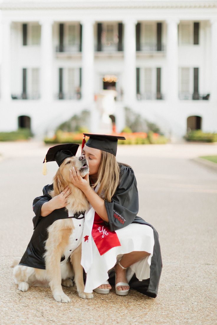 a woman in graduation gown kneeling down next to a dog and holding a graduate's cap