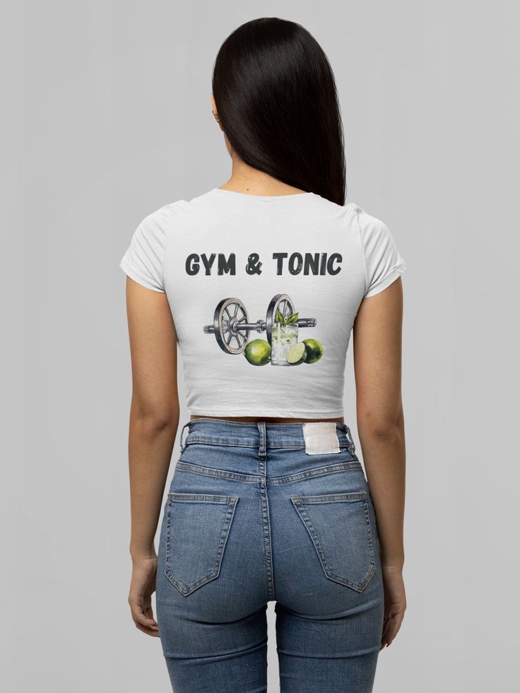 "The T-shirt for gym girls with the slogan \"Gym and Tonic\" combines a playful twist on the classic \"gin and tonic\" with a fitness-oriented theme. It's a fun and witty way to express the idea that hitting the gym is their refreshing tonic and an essential part of their routine, just like a good drink. This shirt is perfect for those who love a dose of humor in their workout attire. This crop top has both comfort and style in spades. Made 100% with silky soft polyester that is both lightweight and breathable." Sports Cotton Crop Top T-shirt, Stretch Sports T-shirt With Text Print, Fitted Sports T-shirt With Graphic Print, Fitted Cropped T-shirt With Graphic Print In Athleisure Style, Sporty Crop Top T-shirt For Workout, Trendy Fitted Cropped T-shirt For Workout, Graphic Print Gym Tops, Graphic Print Gym Tee, Sports Letter Print Crop Top T-shirt