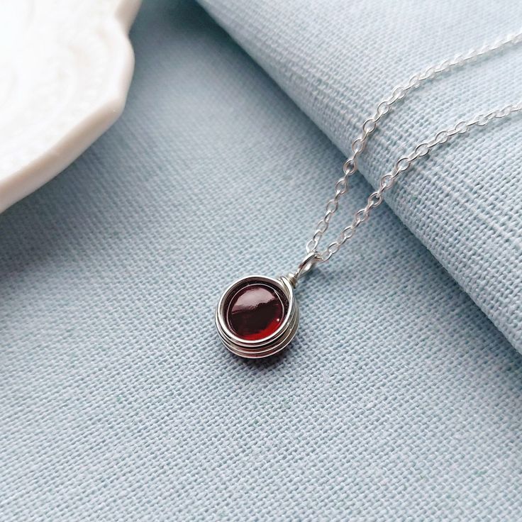 Garnet Necklace, Sterling Silver Necklace, Dainty Necklace, January Birthstone, Birthstone Jewelry DESCRIPTION This minimalist sterling silver necklace features a deep red Garnet cabochon.  The necklace would make a lovely birthday gift for a loved one, close friend or family. Garnet is a birthstone for January. The necklace comes in a lovely fabric pouch as standard. If you would prefer for your jewellery to be presented in a pretty gift box instead, please add it to your order using the drop down menu above.   FEATURES Gemstone: 8mm Natural Garnet Cabochon  Pendant height: 1.5 cm Pendant width: 1 cm Chain: .925 sterling silver chain with soldered links for extra strength Please note that this is a handmade item, so no two are ever exactly alike. Your necklace may look slightly different Sterling Silver Necklace Dainty, Green Onyx Necklace, Fabric Pouch, Peridot Necklace, Garnet Necklace, Onyx Necklace, January Birthstone, Cabochon Pendant, 925 Sterling Silver Chain