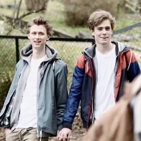 two young men holding hands and walking together