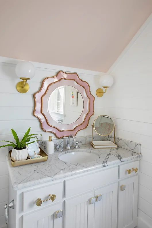 a bathroom with marble counter tops and gold accents on the mirror above it is a plant in a vase