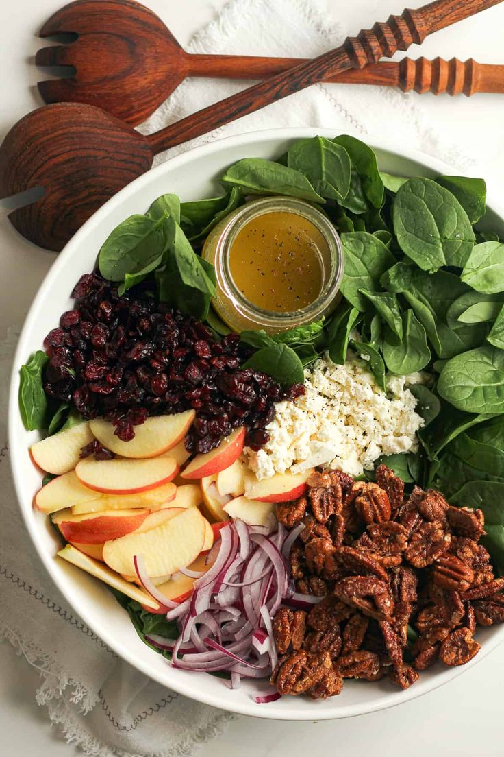 a bowl filled with spinach, apples, cranberry sauce and pecans