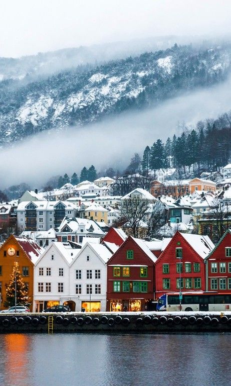 the town is surrounded by snow covered mountains and trees, along with houses on either side