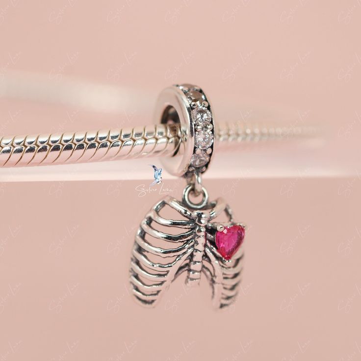 This is charm only, bracelet is sold separately. Experience true love with this exquisite pendant charm featuring a silver rib cage adorned with a stunning pink heart stone. Made of high-quality 925 sterling silver, its polished finish adds a brilliant shine and is accented with a platinum plating. Add this beautiful love oath of rib dangle pendant charm to your bracelet or gift it to your special someone. Materials: 925 sterling silver, cubic zirconiaFinish: platinum plateDimensions: 0.76 x 0.4 Silver Heart Charm Jewelry In Cubic Zirconia, Silver Cubic Zirconia Jewelry With Heart Charm, Dainty Sterling Silver Birthstone Charms, Silver Heart Charms With Dangling Details, Pink Sterling Silver Charm Necklaces, Silver Heart-shaped Dangling Charms, Silver Heart Shaped Dangling Charms, Pink Sterling Silver Charm Necklace, Sterling Silver Dangle Jewelry With Heart Charm