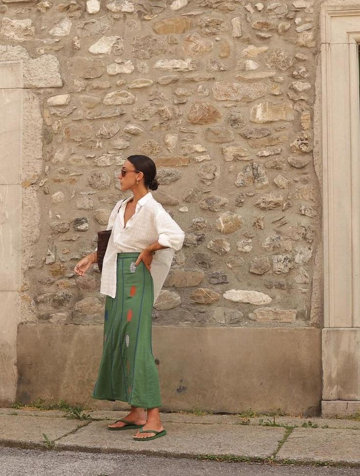 a woman standing in front of a stone building with her hand on her hip and looking up