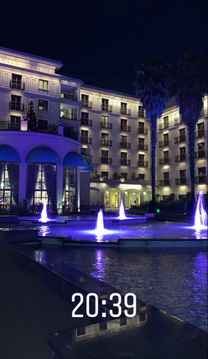 the hotel is lit up at night with blue lights and fountains in front of it