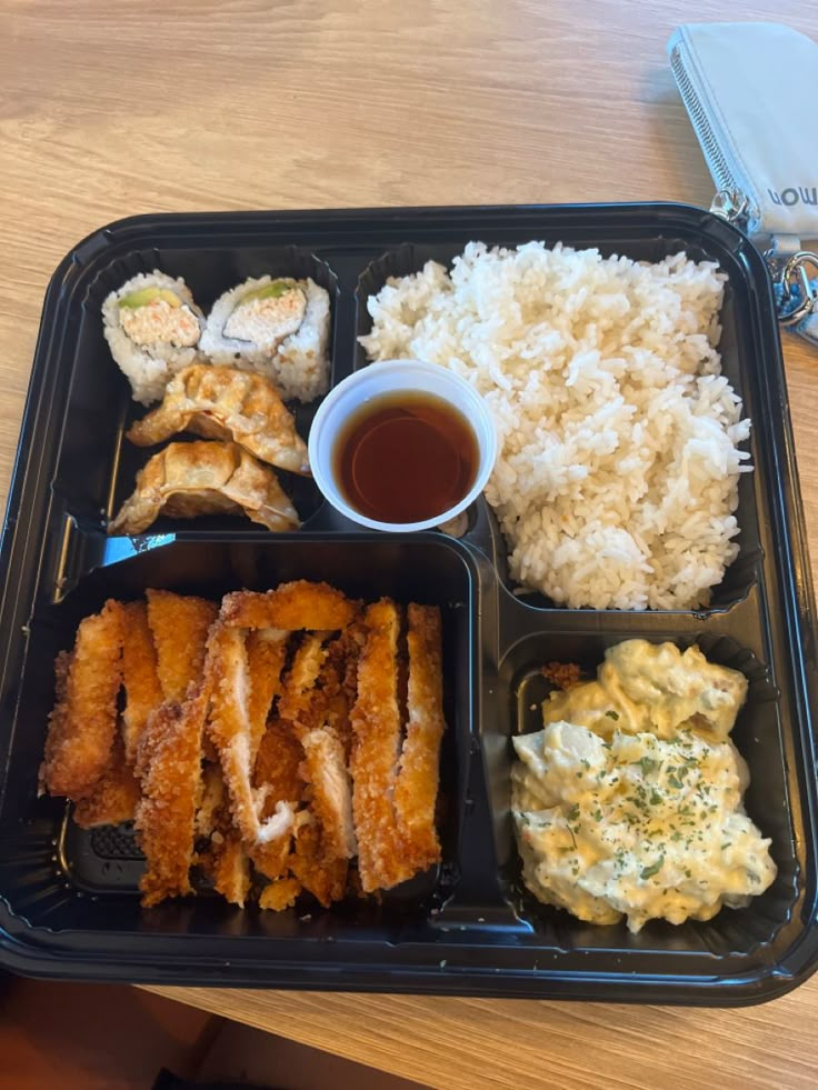 a plastic tray with rice, meat and sauces on it sitting on a wooden table