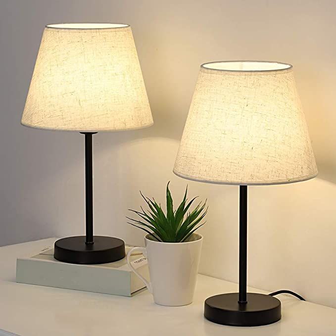 two lamps sitting on top of a white table next to a potted plant and box