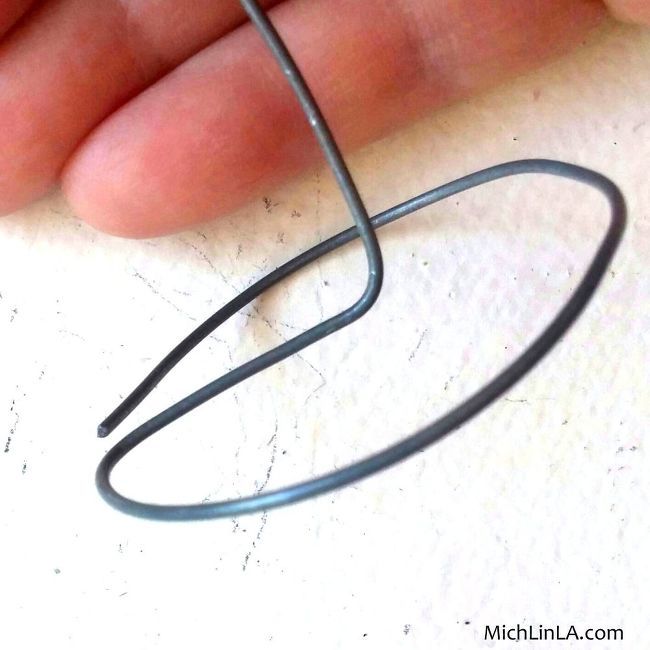 a hand holding a wire that is on top of a white surface with the end of it