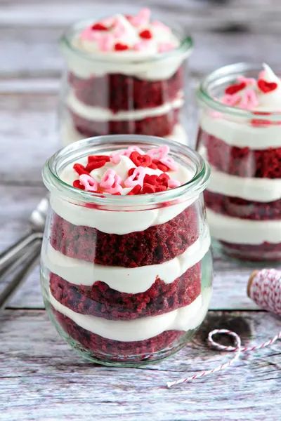 three jars filled with red velvet and white frosting on top of a wooden table