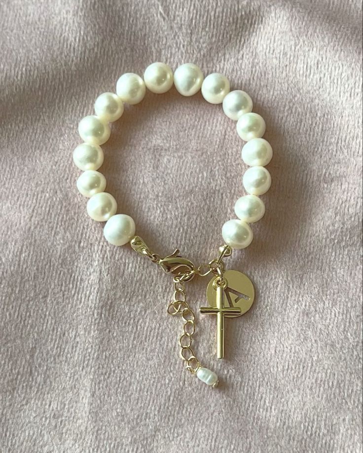 Celebrate important days with the perfect gift: a personalized pearl bracelet. Item Details: Real Freshwater Pearls. 18k Gold Plated Tiny Cross. 18k Gold Plated Initial Letter Charm to make it her very own. What size should you buy? The listing photo shows a 4 1/2” bracelet with an extension chain of 1” It’s always best to measure a bracelet that currently fits the recipient, but if you’re unable to do that, here are some suggestions: Up to 6 months: 4” 6 to 12 months: 4 1/2” 12 mon Elegant Customizable White Jewelry, Customizable Elegant Name Bracelet, Elegant Personalized Pearl Necklace As A Gift, Elegant Personalized Round Bead Jewelry, Elegant Personalized Jewelry With Round Beads, Yellow Gold Round Rosary Bracelet Gift, Elegant White Name Bracelet, Dainty Pearl Bracelet With Pearl Charm For Mother's Day, Pearl Drop Bracelet Perfect As A Gift