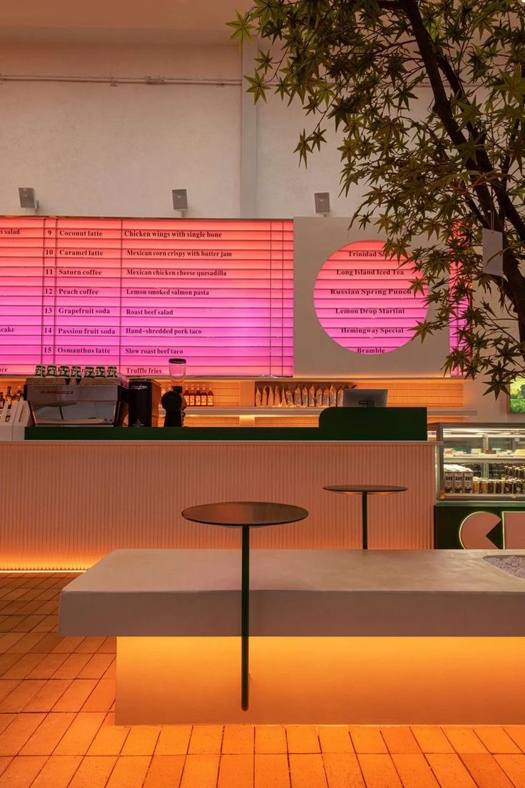 the interior of a restaurant with tables and stools in front of a large pink screen