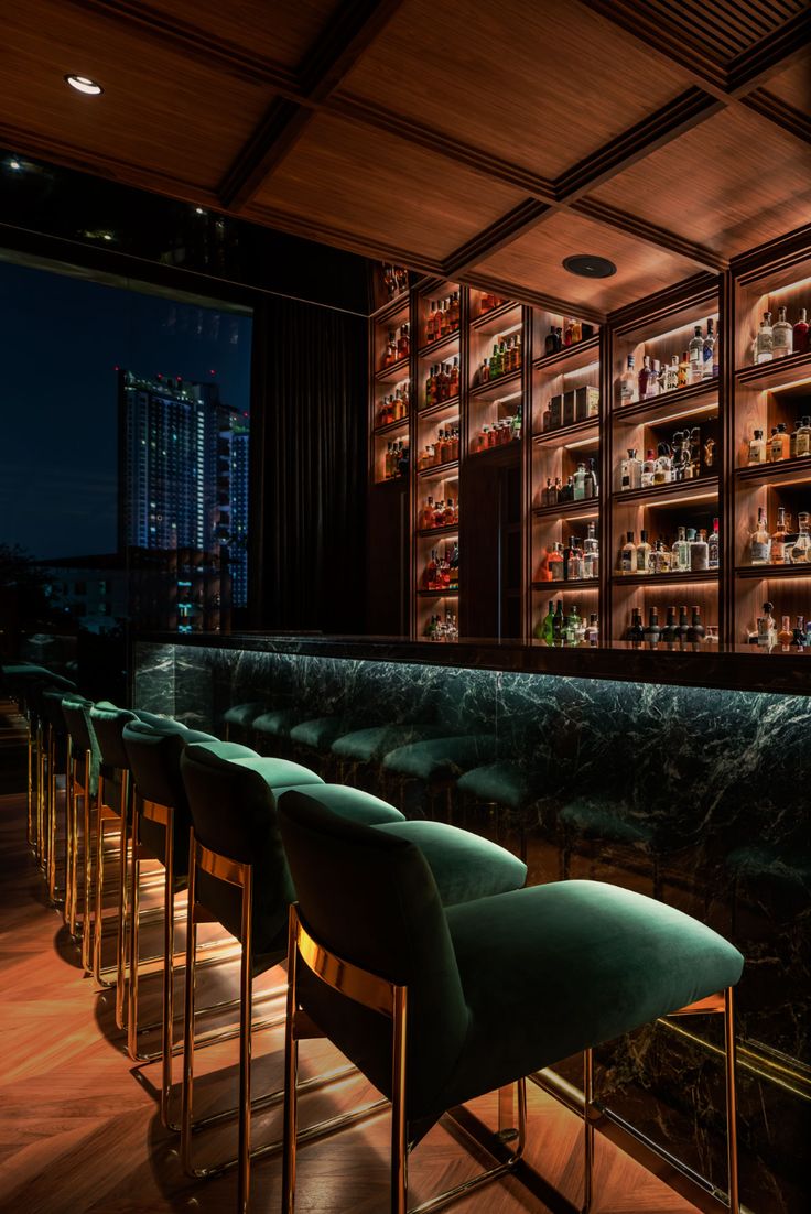 a dimly lit bar with green velvet chairs