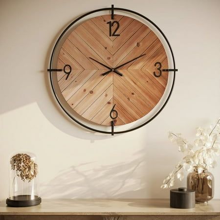 a large wooden clock on the wall above a table with vases and flowers in front of it