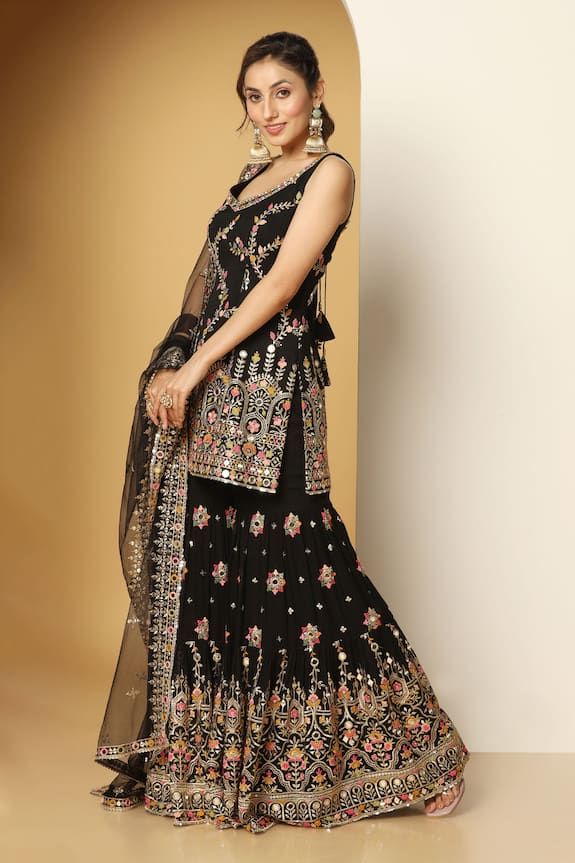 Black sleeveless padded short kurta in georgette base with all over mughal bloom art multi color thread, zari, mirror embroideries, sequin highlights and paan neckline. Paired with a floral motif embroidered sharara and mirror border embellished net dupatta. - Aza Fashions Sleeveless Cutdana Salwar Kameez For Festivals, Sleeveless Traditional Wear With Mirror Work, Traditional Sleeveless Salwar Kameez With Mirror Work, Sleeveless Mirror Work Sets For Eid, Traditional Sleeveless Sets With Mirror Work, Sleeveless Eid Sets With Mirror Work, Sleeveless Chinon Dresses For Eid, Sleeveless Georgette Salwar Kameez With Mirror Work, Sleeveless Georgette Sharara With Mirror Work