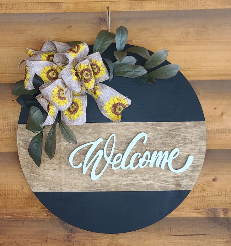 a welcome sign hanging on the side of a wooden wall with sunflowers and leaves