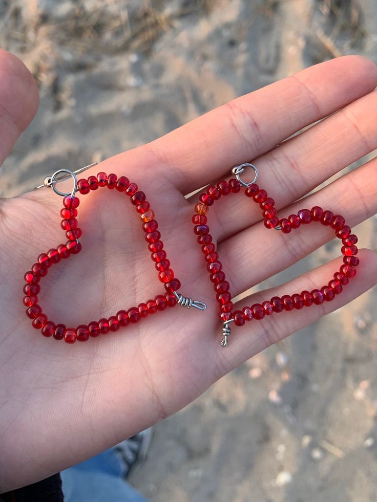 a hand holding two red beads in the shape of a heart