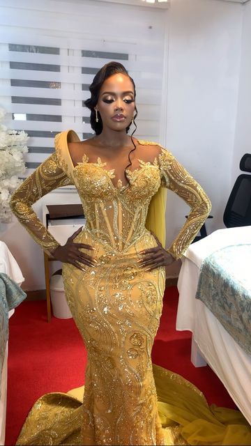 a woman standing in front of a bed wearing a gold gown