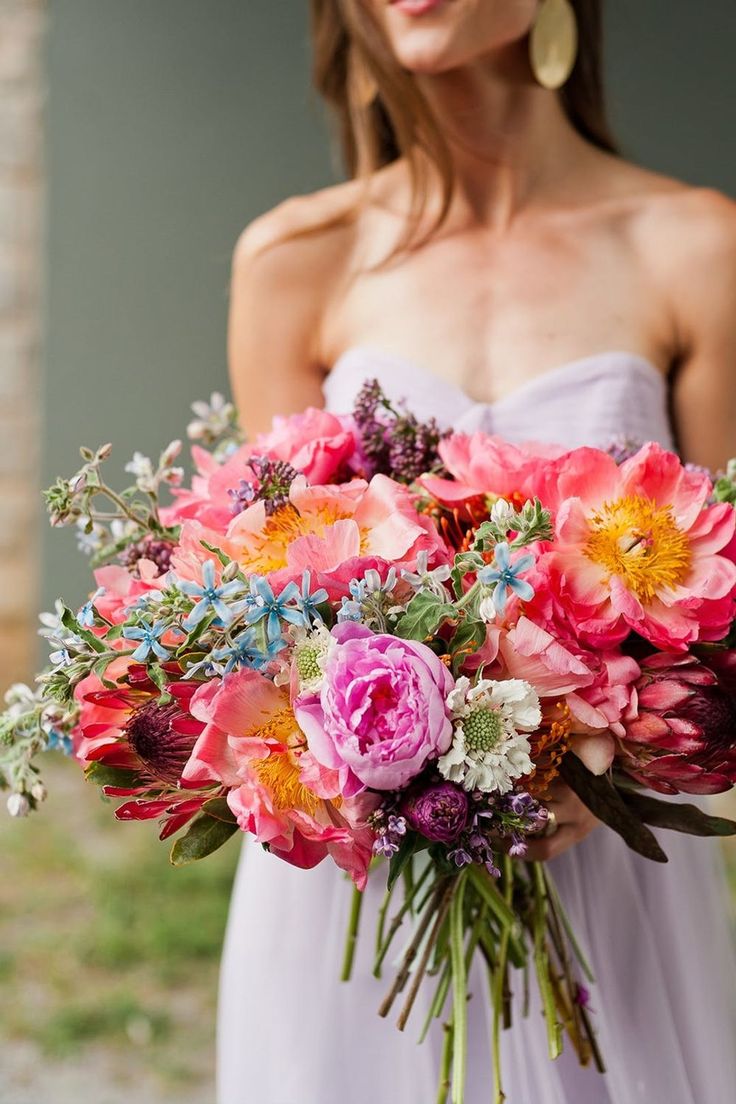 a woman in a white dress holding a large bouquet of pink, orange and yellow flowers