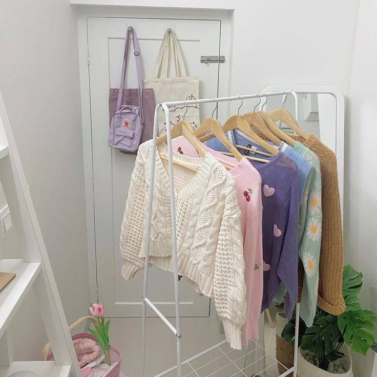 several sweaters and handbags are hanging on a rack next to a potted plant