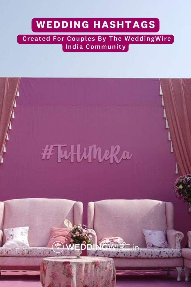 a couch and table in front of a pink wall with the words wedding hashtags written on it