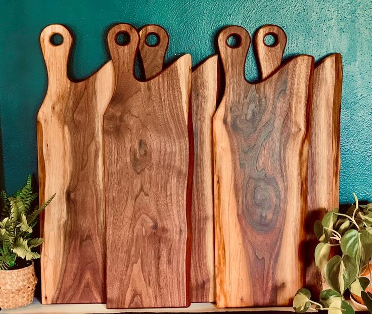 three wooden cutting boards sitting on top of a shelf next to a potted plant