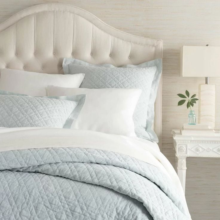 a bed with white and blue comforters in a bedroom next to a night stand