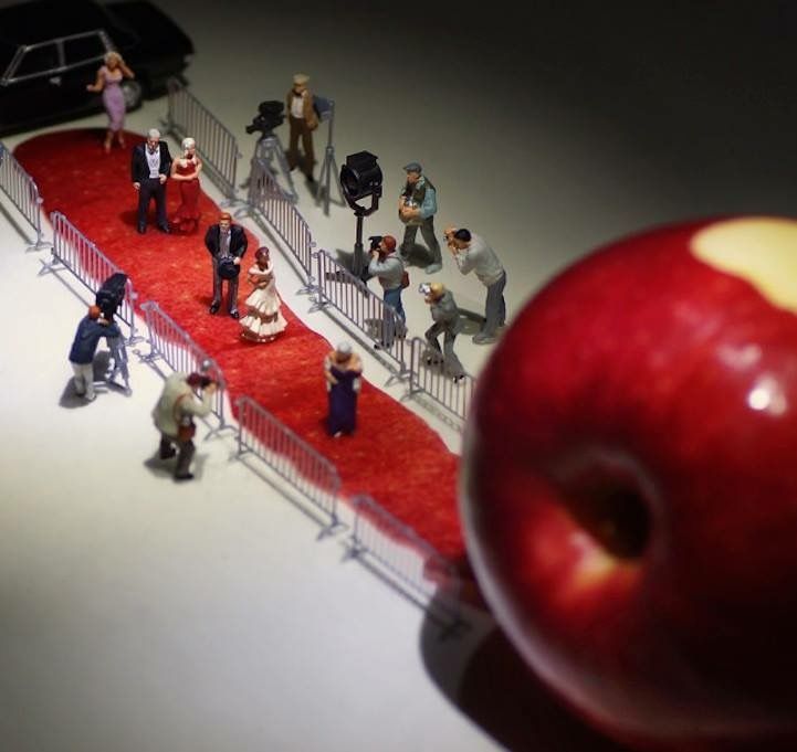 miniature people are standing on a red carpet next to an apple