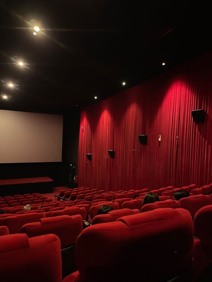 an empty movie theater with red seats and projector screen on the wall, at night