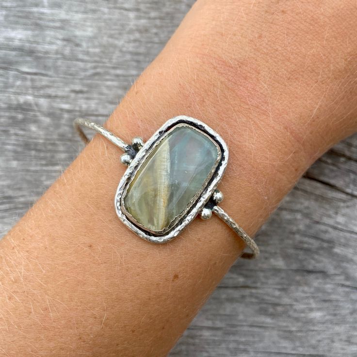 Sterling silver aquateen cuff. Hand made with love! The aquateen has a smooth finish and the silver outline is rather rough, giving the cuff an organic and natural touch. Cuff width: 65 mm (slightly adjustable) Gemstone height: 28mm Gemstone width: 18mm Take a look at our Pebbles & Chance ETSY store https://www.etsy.com/es/shop/pebblesandchance to combine it with other unique, raw, beautiful, precious pieces! Follow us on Instagram! https://www.instagram.com/pebblesandchance/?hl=es Unique Hand Forged Bangle Jewelry, Spiritual Hand Forged Cuff Bracelet Gift, Adjustable Sterling Silver Jewelry With Large Stone, Adjustable Sterling Silver Bangle Jewelry, Hand Wrapped Bangle Jewelry As Gift, Hand Wrapped Bangle Jewelry For Gifts, Sterling Silver Gemstone Bangle, Sterling Silver Bangle Bracelet With Natural Stones, Sterling Silver Hand Wrapped Bangle