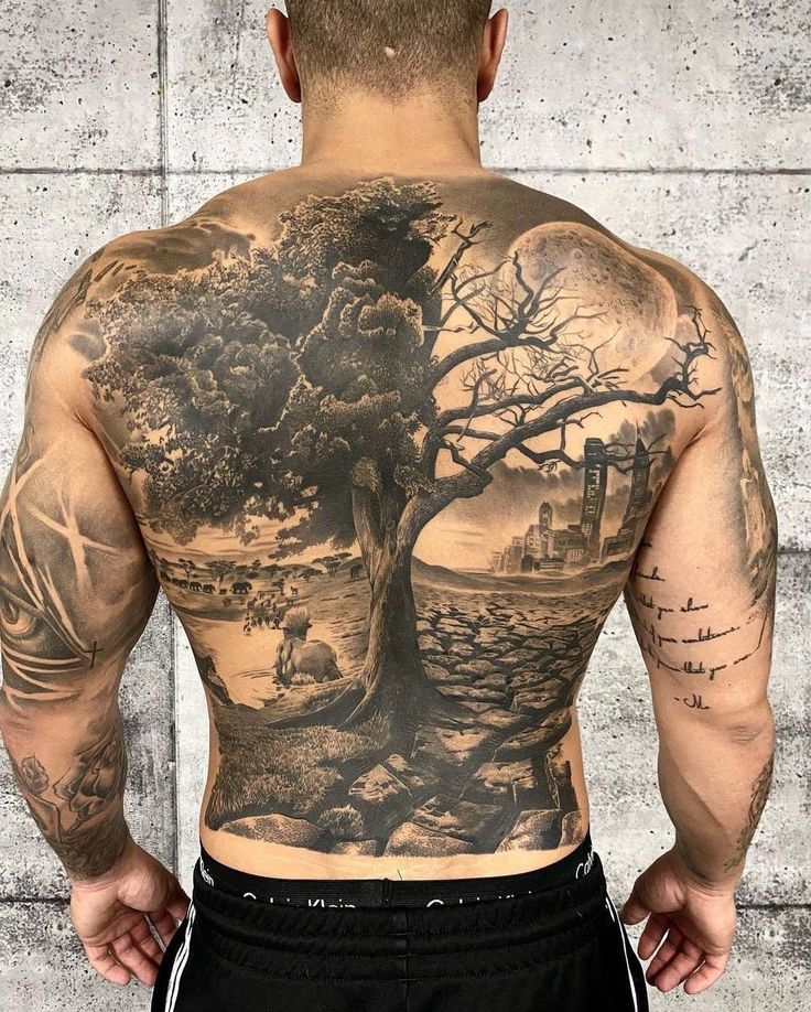 a man with tattoos on his back is standing in front of a wall and looking at the tree