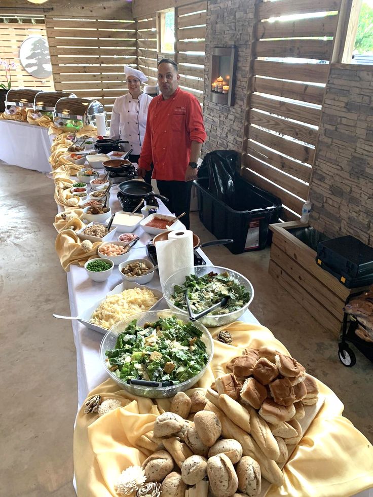 several people are standing at a buffet line with food on the table in front of them