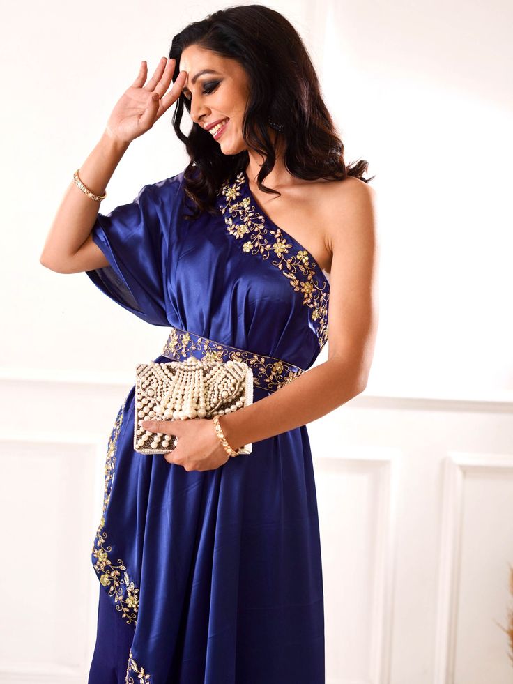 A four-piece Sehar Navy Amber Cape Sharara set from the Rashika Sharma collection. This beautiful navy blue flared sharara pants in chiffon fabric is paired with an embroidered satin one-shoulder cape. The outfit is completed with an embroidered waist belt and an inner satin bustier. The beads, zari, sequins, mirror and resham work enhance the Sehar Navy Amber Cape Sharara set.
Clutch NOT included. Evening Kaftan With Dupatta, Traditional One-shoulder Festive Sets, Festive Traditional One-shoulder Set, Silk Kaftan With Zari Work For Evening, Traditional One-shoulder Embroidered Dress, Evening One Shoulder Dress With Zari Work, Evening One-shoulder Dress With Zari Work, One Shoulder Evening Dress With Zari Work, Festive One Shoulder Silk Dresses