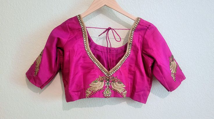 Royal rich pink/fuschia pure silk (pattu) saree blouse with beautiful jewelry work of kundans, gold zari dabka pitta, zardosi hand embroidery.  Resembling the deep gemstone pink in the color with majestic and elegant jewel hand work, this blouse is for sure to turn heads for its royal and graceful look.  Padded blouse Backside dories Peacocks are one of the most beautiful birds in the world, so it's no wonder they symbolize beauty, glamour, and majesty. The gorgeous design of embroidery for the neck line and sleeves is beautiful and intricate that it will make you fall in love with the blouse at the first sight.  Size 38 and can be opened upto 42 Elegant Pink Choli With Pallu, Pink Blouse With Mirror Work In Traditional Drape, Pink Blouse With Mirror Work And Traditional Drape, Pink Silk Choli With Mirror Work, Elegant Pink Chanderi Choli, Elegant Pink Choli With Cutdana, Elegant Pink Choli With Mirror Work, Elegant Pink Cutdana Choli, Gold Blouse Piece With Mirror Work In Raw Silk