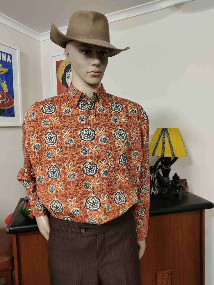 This bright Indian cotton shirt is in a fun print in colours of orange pale yellow and grey in an abstract floral. The shirt has long sleeves and a chest pocket and is in a extra large size by Trinity label.  The condition is very good. Measurements are Shoulder to shoulder 54cm Chest 132cm Sleeves shoulder to cuff 59cm Length shoulder to hem 80cm Long Sleeve Printed Shirt For Fall, Printed Long Sleeve Shirt For Fall, Multicolor Print Long Sleeve Shirt For Fall, Fall Long Sleeve Printed Shirt, Multicolor Graphic Print Long Sleeve Shirt, Fall Long Sleeve Shirt With Abstract Print, Fitted Long Sleeve Orange Shirt, Fitted Orange Long Sleeve Shirt, Retro Long Sleeve Shirt With Retro Print