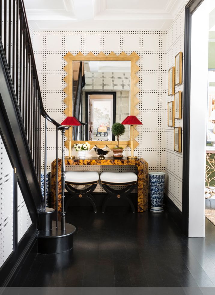 the hallway is decorated with black and white wallpaper, gold trimmings, an ornate console table, and two red lamps on either side tables