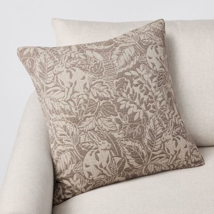 a white couch with a brown floral pillow on it's back and the seat up