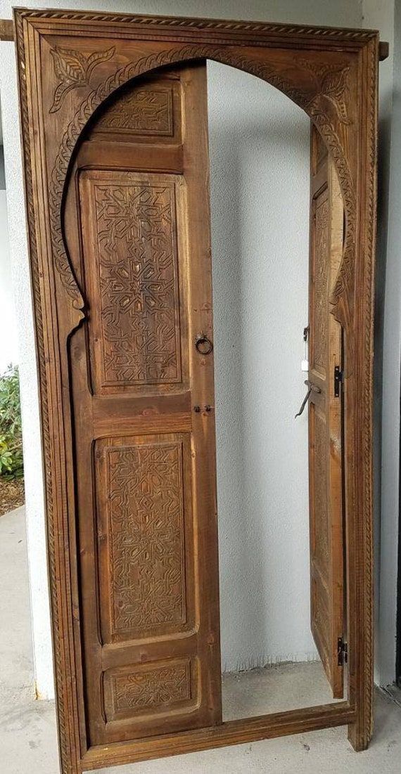 an open wooden door with intricate carvings on the outside and inside, in front of a white wall