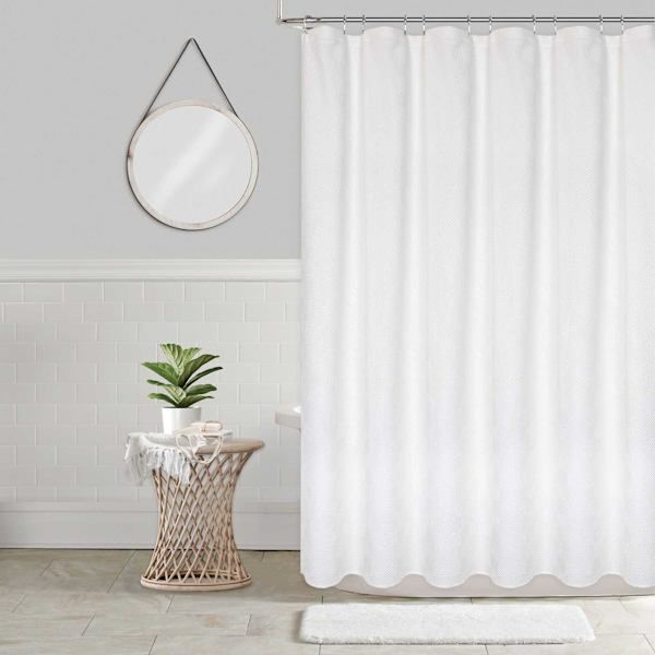 a white shower curtain in a bathroom next to a potted plant and round mirror