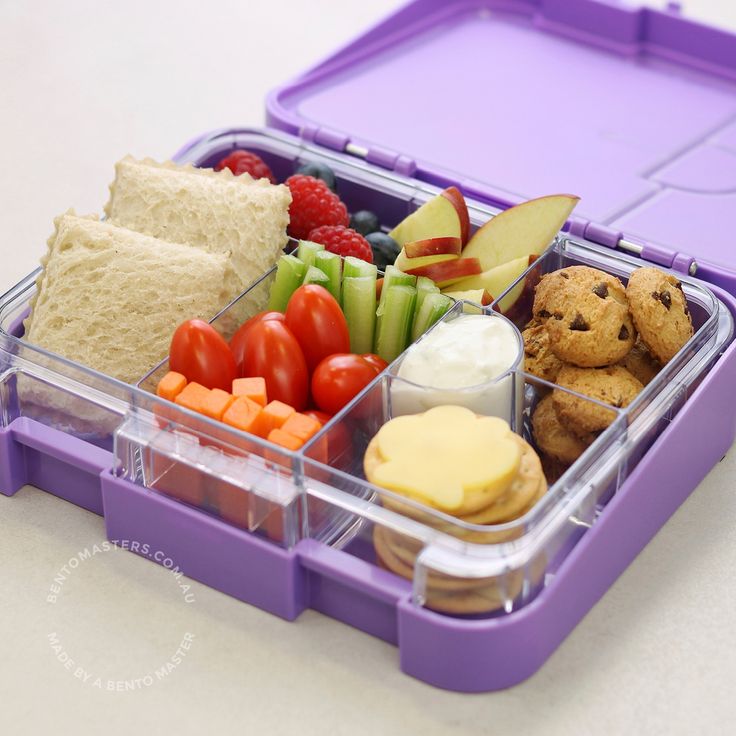 a plastic container filled with food on top of a white table next to a purple tray